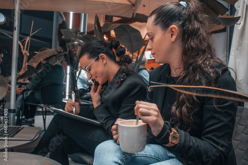 Compañeras de trabajo con seriedad llamando por telefono movil y escribiendo planteamientos junto su ordenador laptop en una cafeteria de su ciudad tomando café por la mañana para terminar su trabajo photo