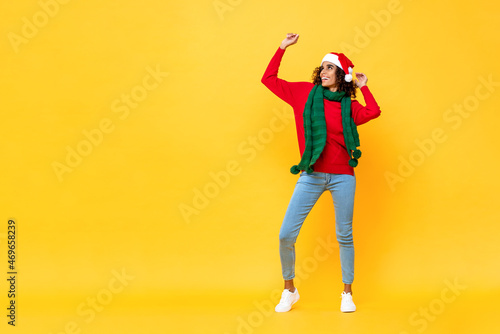 Full length portrait of fun happy Afircan American woman in Christmas attire dancing on isolated yellow studio background with copy space