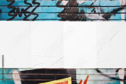 Closeup of colorful messy painted urban wall texture with four wrinkled glued poster templates. Modern mockup for design presentation with clipping path. Creative urban city background. 