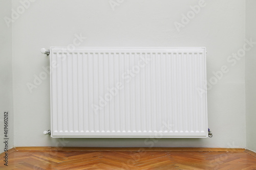 Home radiator heater on the white wall on wooden hardwood floor. Adjustable warming equipment for apartment and home 