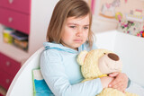 Cute little caucasian crying girl with teddy bear in bedroom. Sad unhappy children emotions