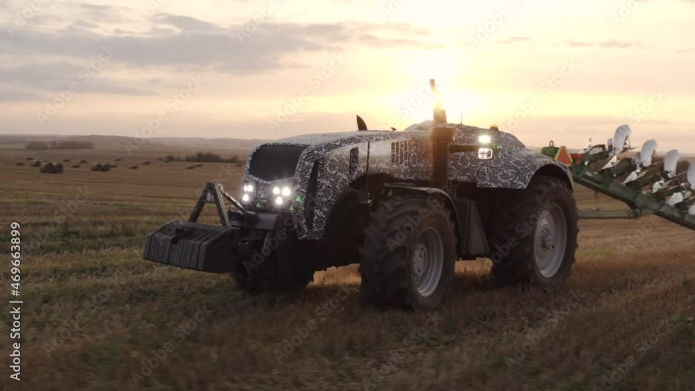 An unmanned tractor drives through a field and plows the land with a plow at sunset An unmanned tractor drives through a field and plows the land with a plow at sunset