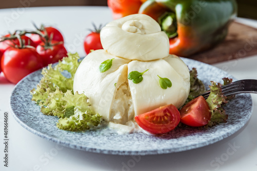 Fresh handmade soft Italian cheese, white balls of burrata or burratina cheese made from mozzarella and cream filling with lettuce leaves and red tomatoes