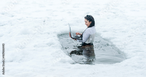 Girl with laptop in frozen lake ice hole. Woman hardening the body in cold water. Good immunity is protection against many diseases.