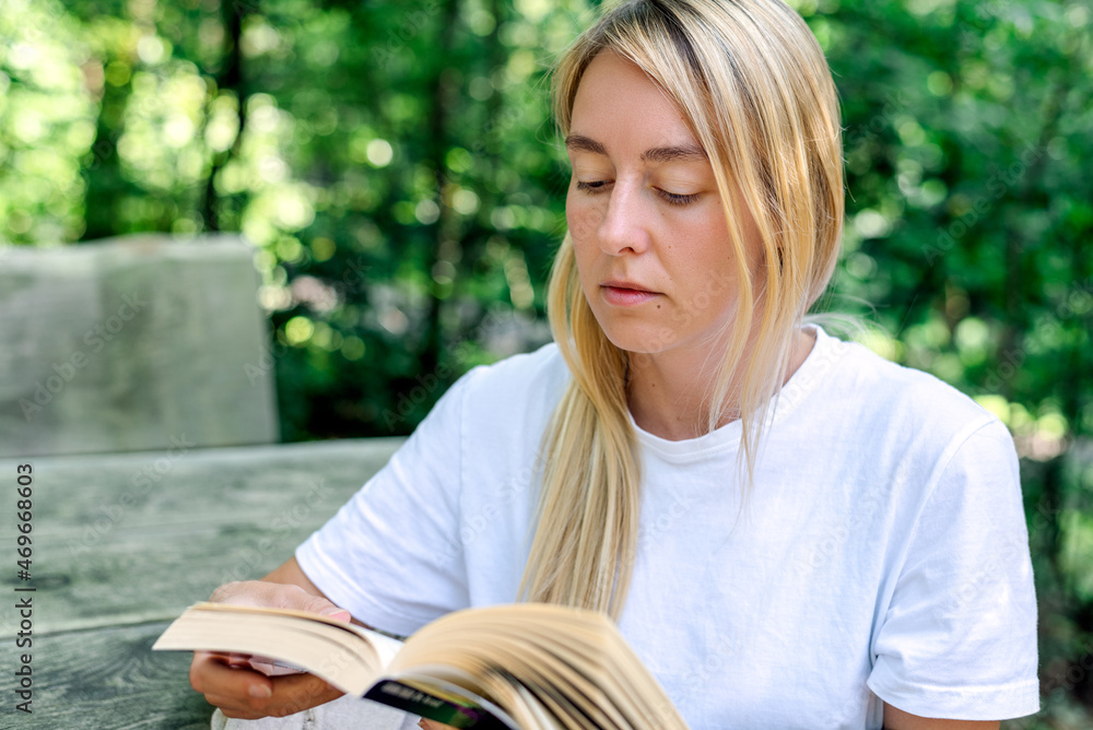 A young woman reads a book outdoors. A young woman reads a book outdoors.