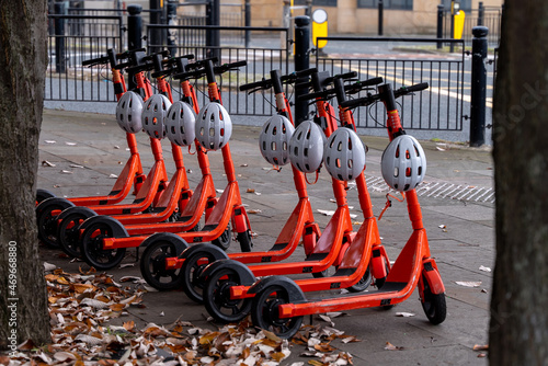 Line of orange electric scooters with white helmets hanging off
