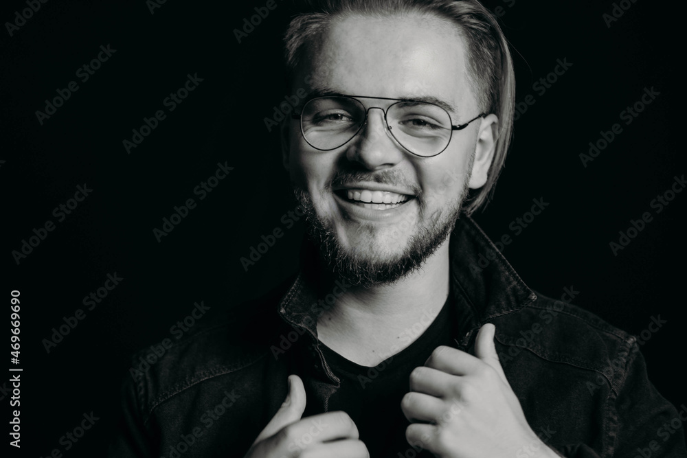 Fototapeta premium Black and white photo of young attractive guy laughing sincerely. Portrait of happy man with wide smile with teeth. Charismatic cute male with round glasses and modern stylish haircut. Studio shooting