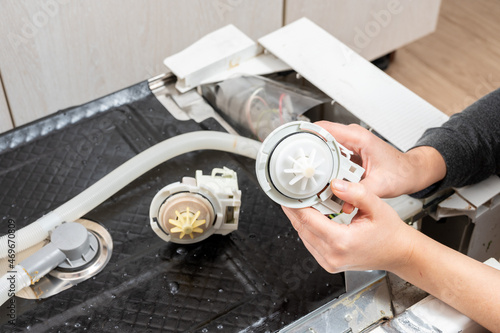 A new pump for a dishwasher in the hands of a woman, against the background of a disassembled dishwasher