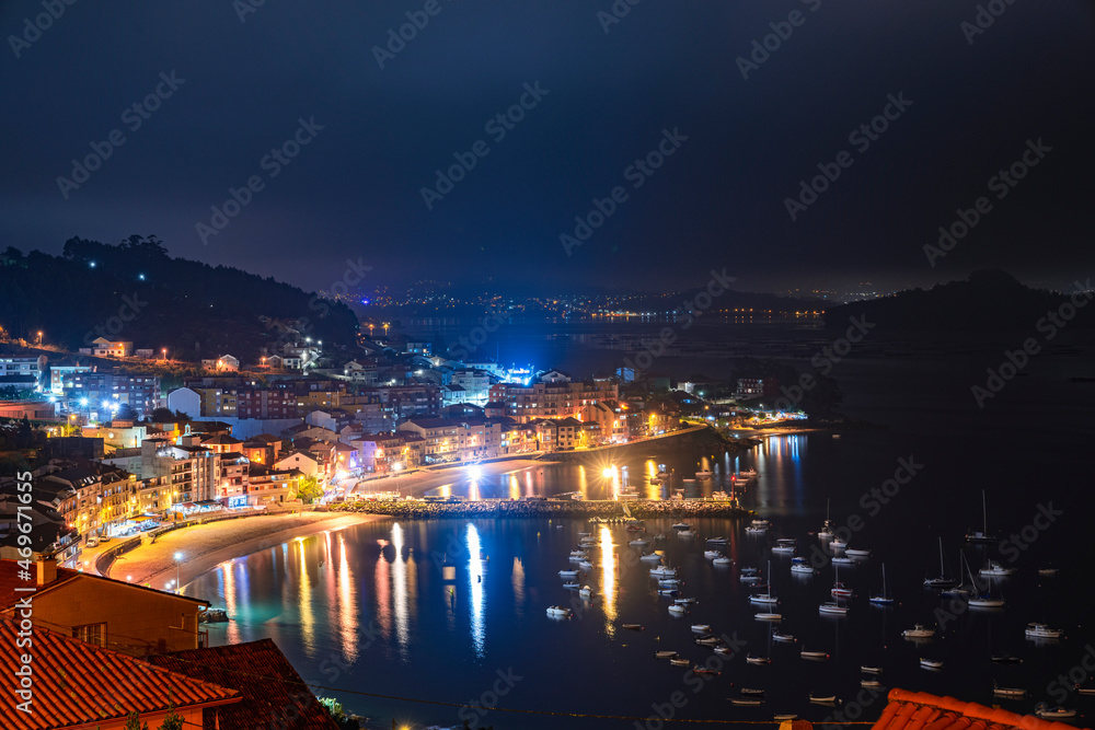 Pueblo costero de noche  en la ría de Pontevedra con playa y barcos en el puerto iluminado