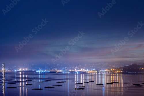 Ría de Pontevedra de noche y bateas de mejillones y ciudad de fondo con luces.