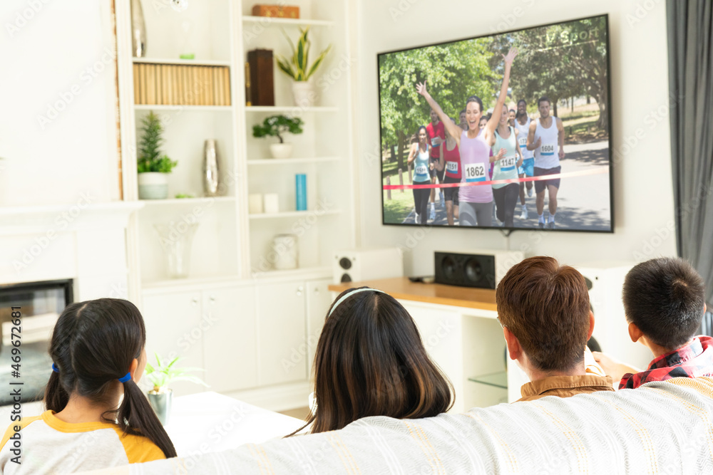 Rear view of family sitting at home together watching athletics event on tv Rear view of family sitting at home together watching athletics event on tv