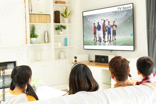 Rear view of family sitting at home together watching sport event on tv
