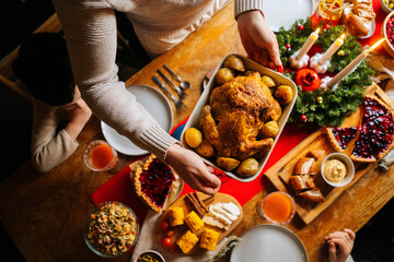 Close-up top view of young father male putting dish with baked hot turkey on holiday dinner table served for Christmas family party, celebrating thanksgiving day with roasted turkey for dinner.