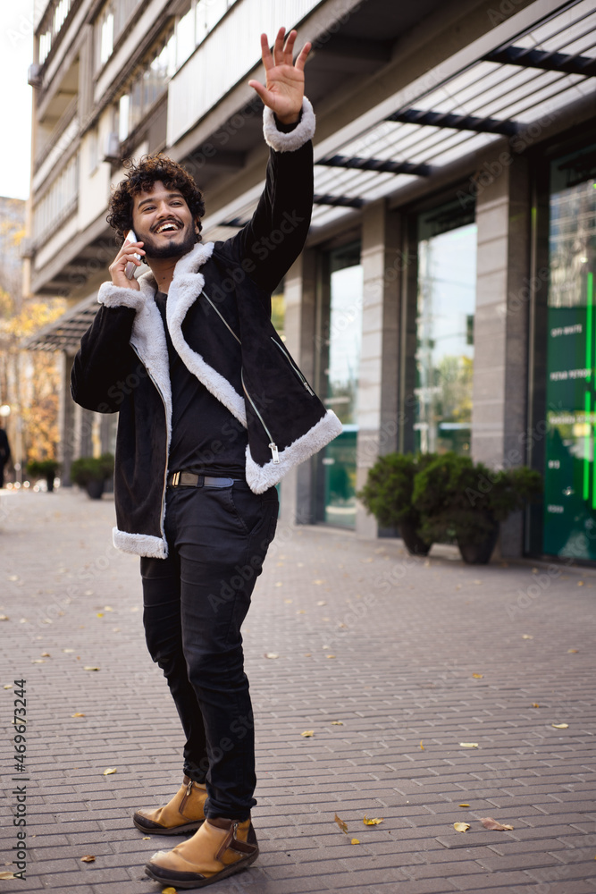 Smiling indian man waving hand while talking on smartphone on street Smiling indian man waving hand while talking on smartphone on street