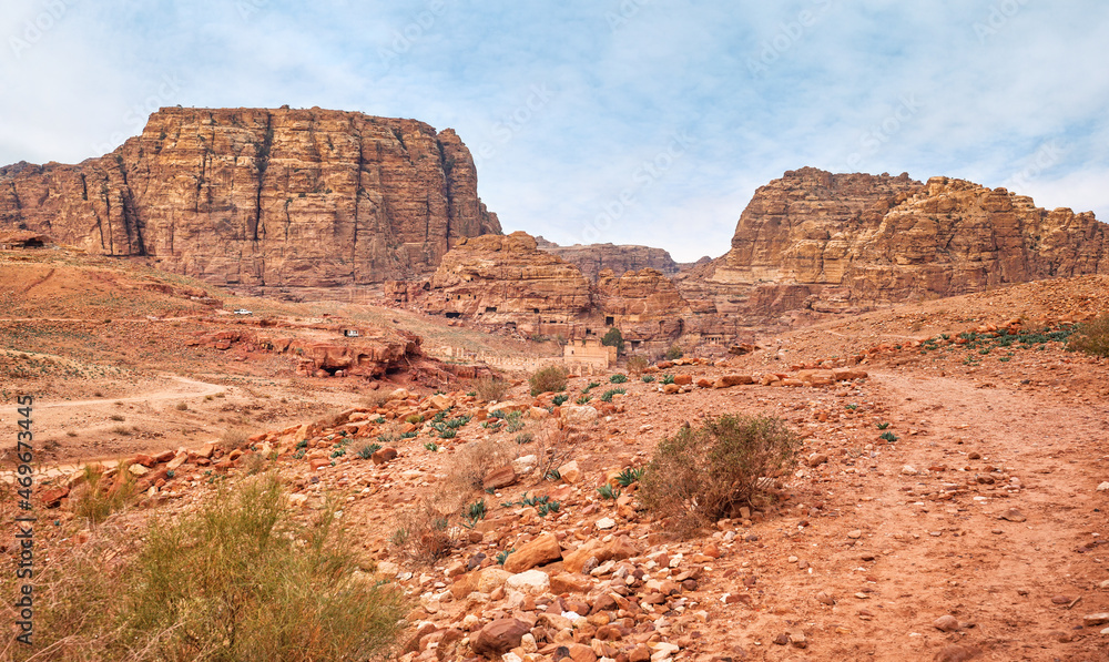 Typical landscape at Petra, Jordan, red dusty ground, mountains with carved buildings inside in distance Typical landscape at Petra, Jordan, red dusty ground, mountains with carved buildings inside in distance