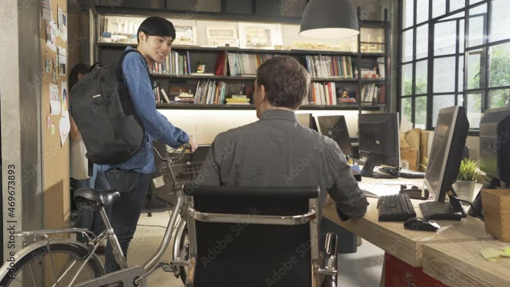 An Asian man, employee comes back to work by bike or bicycle and say hello to a Western man boss at office workplace. Greeting and welcoming. People lifestyle An Asian man, employee comes back to work by bike or bicycle and say hello to a Western man boss at office workplace. Greeting and welcoming. People lifestyle
