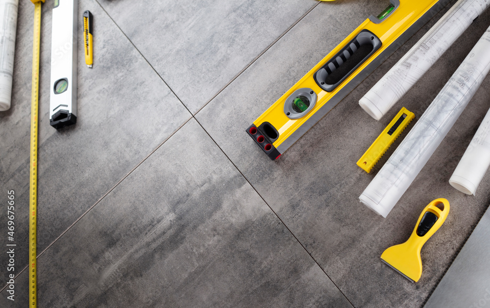 Contractor theme. Tool kit of the contractor: yellow hardhat, libella, hand saw. Plans and notebook on the gray tiles background.