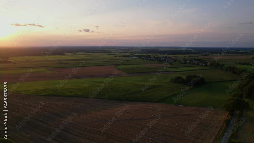 Aerial view of sunset over the agriculture fields in a summer evening. Blue sky with pastel pink clouds. Slow drone flight over the green fields and hay bales. Aerial view of sunset over the agriculture fields in a summer evening. Blue sky with pastel pink clouds. Slow drone flight over the green fields and hay bales.