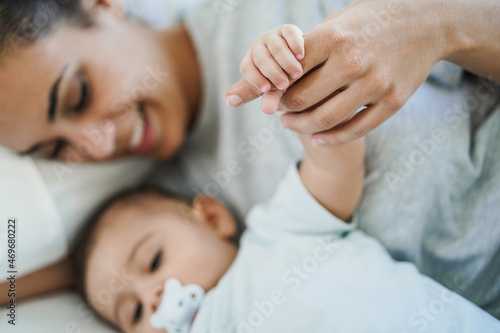 Young mother holding her baby hand while lying on bed at home - Family, motherhood and love concept