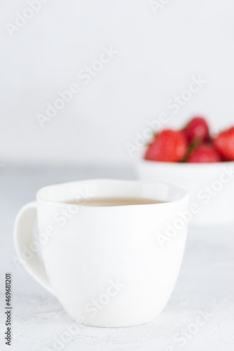 A cup of tea with ripe strawberries on a light table. Selective focus.