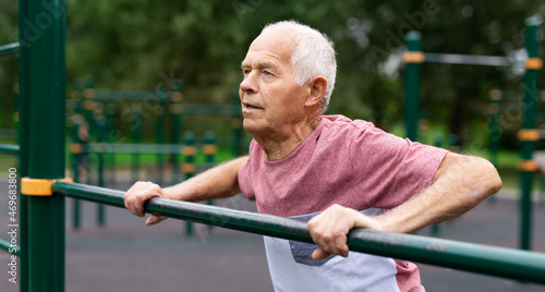 Elderly man doing fitness on sports ground equipment in park