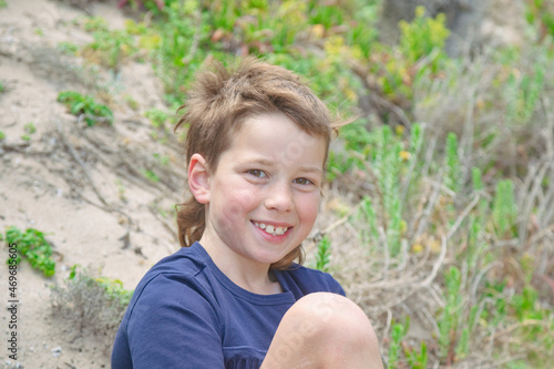 Aussie boy with mullet sitting on sand dune at the beach