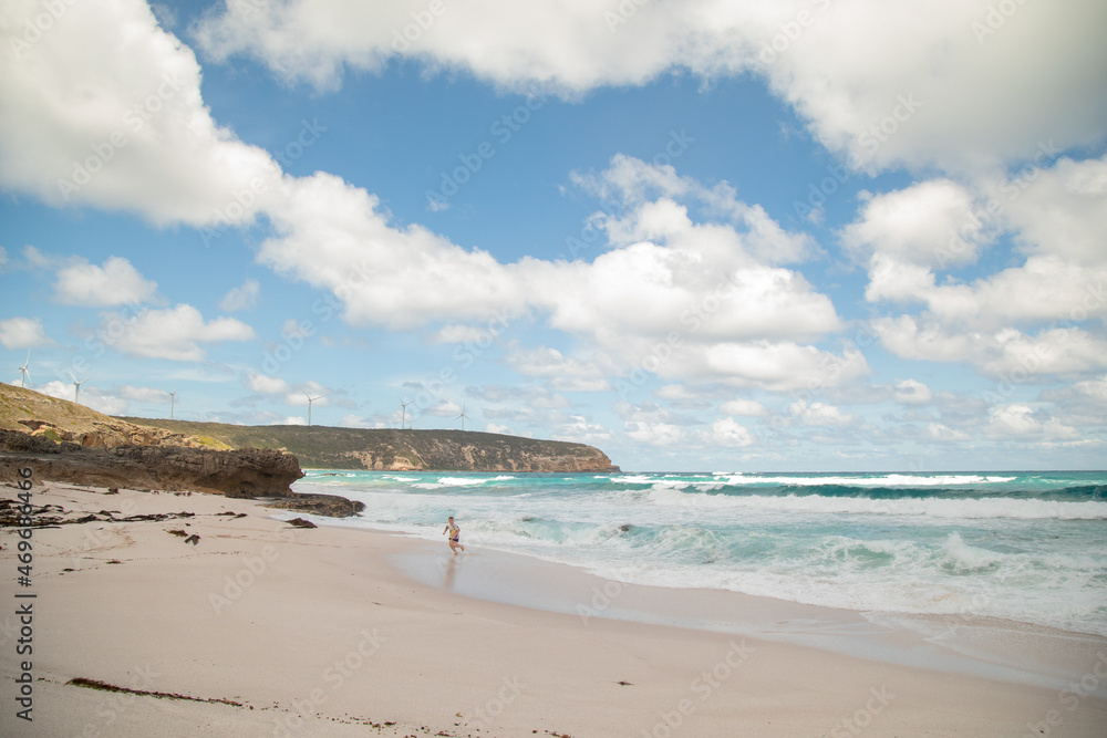 Boy running from waves on the beach with wind turbines on cliff in the background Boy running from waves on the beach with wind turbines on cliff in the background