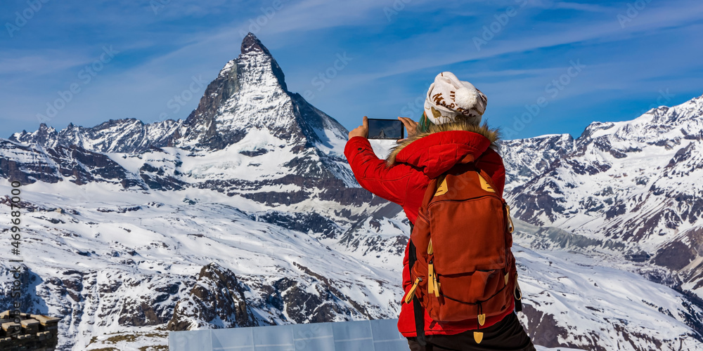 Back view of young woman tourist in red cloth using smartphone taking apicture in Matterhorn mountain ,Swiss apls