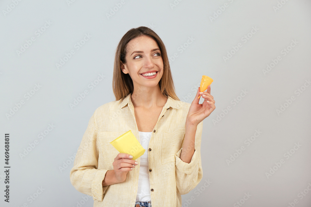 Happy young woman with menstrual cup and disposable pad on grey background Happy young woman with menstrual cup and disposable pad on grey background