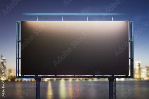 Blank black billboard on city buildings background at night, front view. Mockup, advertising concept