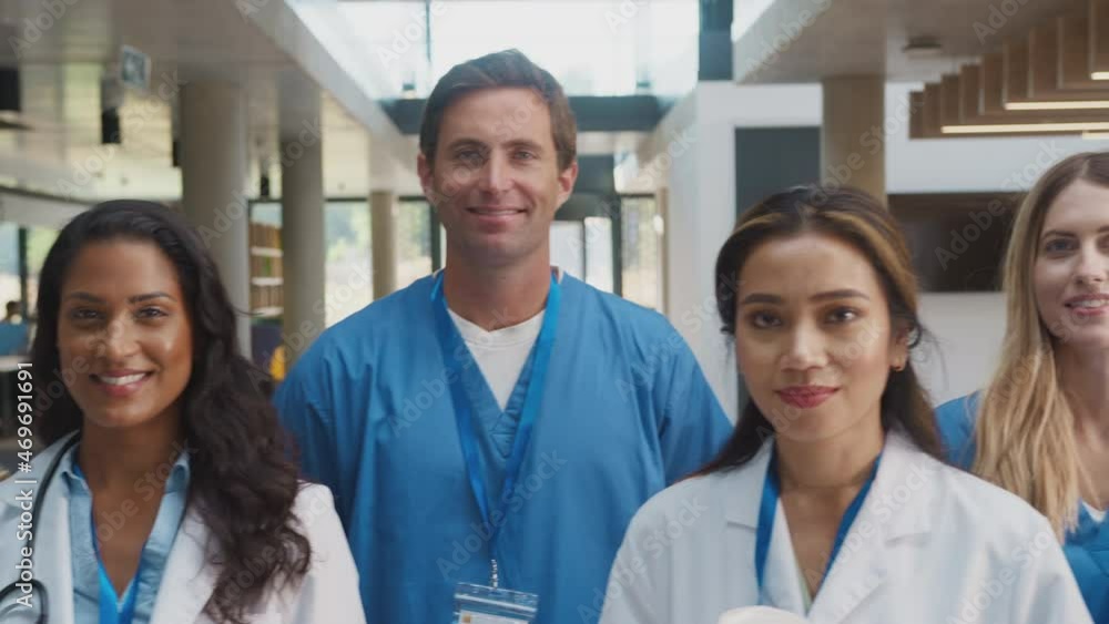 Camera tracks along faces of multi-cultural medical team wearing uniform standing inside hospital building smiling at camera - shot in slow motion Camera tracks along faces of multi-cultural medical team wearing uniform standing inside hospital building smiling at camera - shot in slow motion