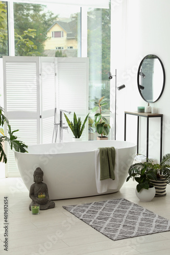 Stylish bathroom interior with modern tub, window and beautiful houseplants. Home design
