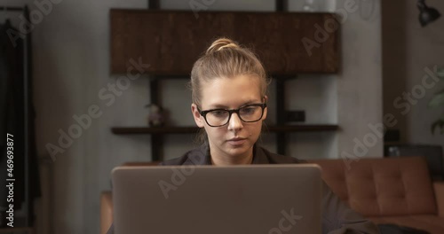 Woman student in eyeglasses concentrated working with laptop, background of minimalist room. Portrait of smart woman with device working. Concept of distance learning