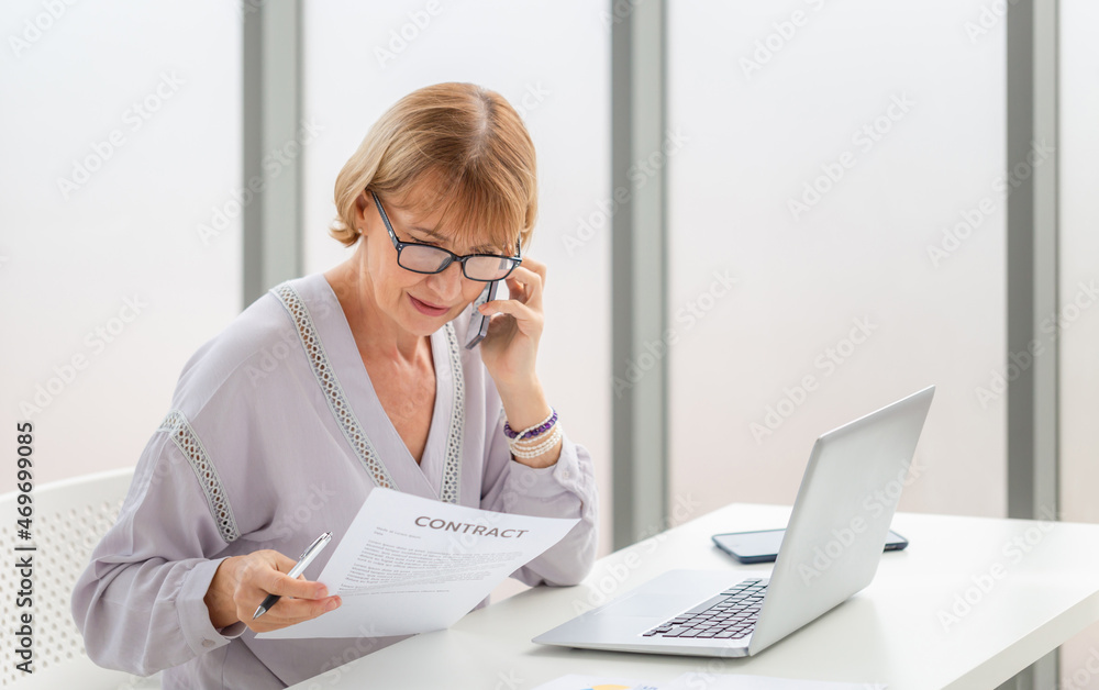 Portrait of woman using laptop and smartphone working from home, Mature casual woman working on a laptop in living room Portrait of woman using laptop and smartphone working from home, Mature casual woman working on a laptop in living room