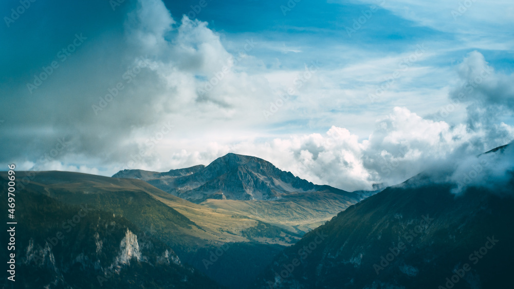 A mountain gorge covered with a forest. A mountain with a glacier rises in the background. White clouds cling to the mountains. Blue sky in the background. The beauty of nature. A mountain gorge covered with a forest. A mountain with a glacier rises in the background. White clouds cling to the mountains. Blue sky in the background. The beauty of nature.