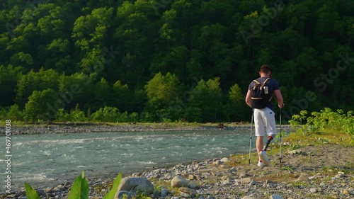male traveller with disabilities is walking alone over mountain river shore