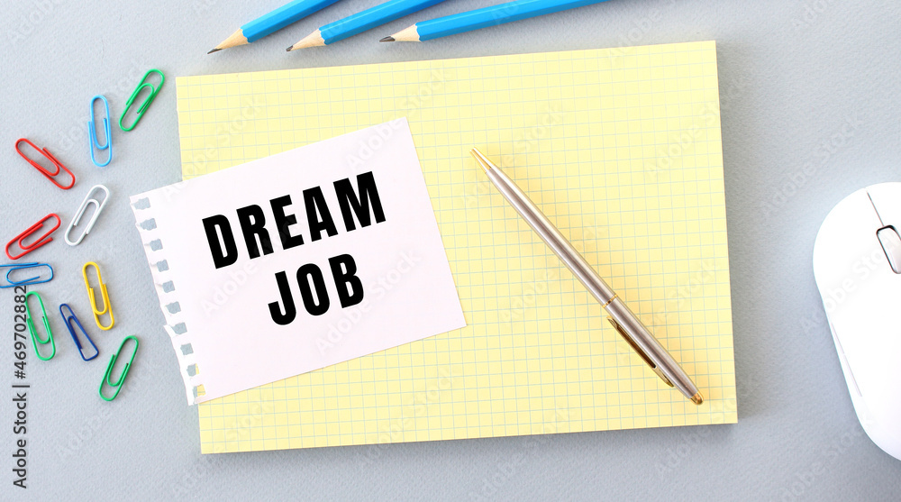 DREAM JOB is written on a piece of paper that lies on a notebook next to office supplies. DREAM JOB is written on a piece of paper that lies on a notebook next to office supplies.