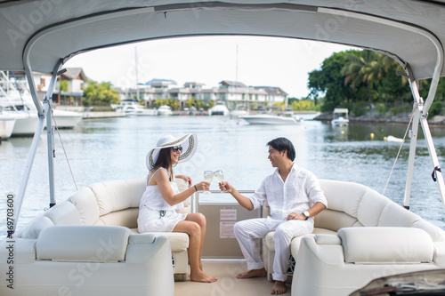 Smiling young couple holding glasses with champagne and looking at each other while sitting on the board of yacht © Artem Zakharov
