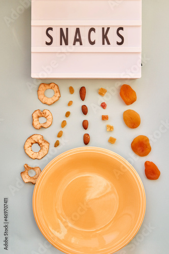 Splash of dry fruits apple slices, dried apricots, almonds, candied fruit and raisins. Proper nutrition, healthy food, snacks concept. Mock up of empty plate. Text snacks. Template for design