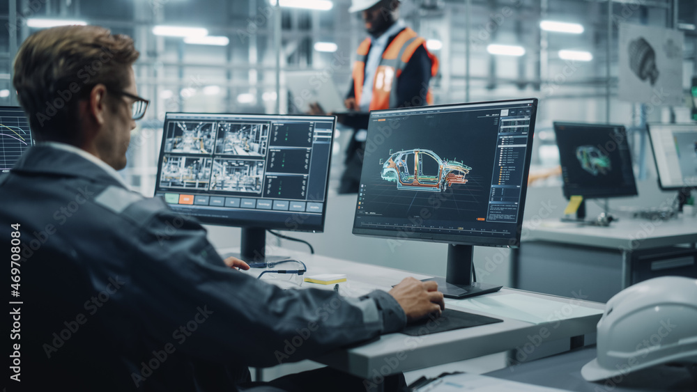 Vehicle Factory Line Operator Working at Desk, Overviewing Autonomous Electric Car Production. In the Background African American Engineer Using Tablet and Looking at a Car Assembly Plant.  - obrazy, fototapety, plakaty 