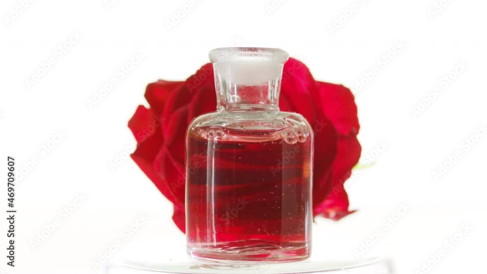 Rose oil is pouring into old fashioned reagent bottle creating bubbles in front of red rose flower on white background | Abstract skincare cosmetics with rose oil mixing concept Rose oil is pouring into old fashioned reagent bottle creating bubbles in front of red rose flower on white background | Abstract skincare cosmetics with rose oil mixing concept