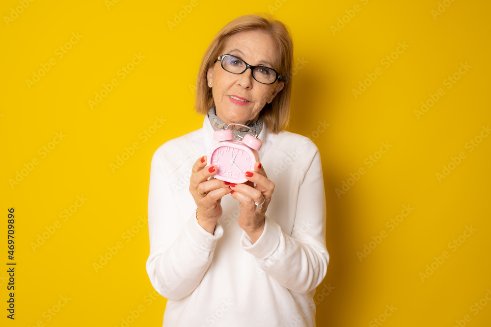 Mature woman showing clock isolated over yellow background. Mature woman showing clock isolated over yellow background.