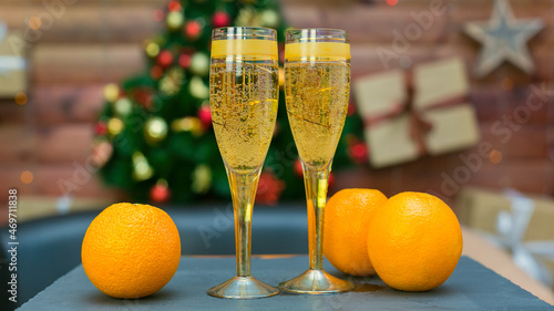 Two glasses of champagne and bright juicy oranges on the background of an elegant Christmas tree, the concept of the new year.