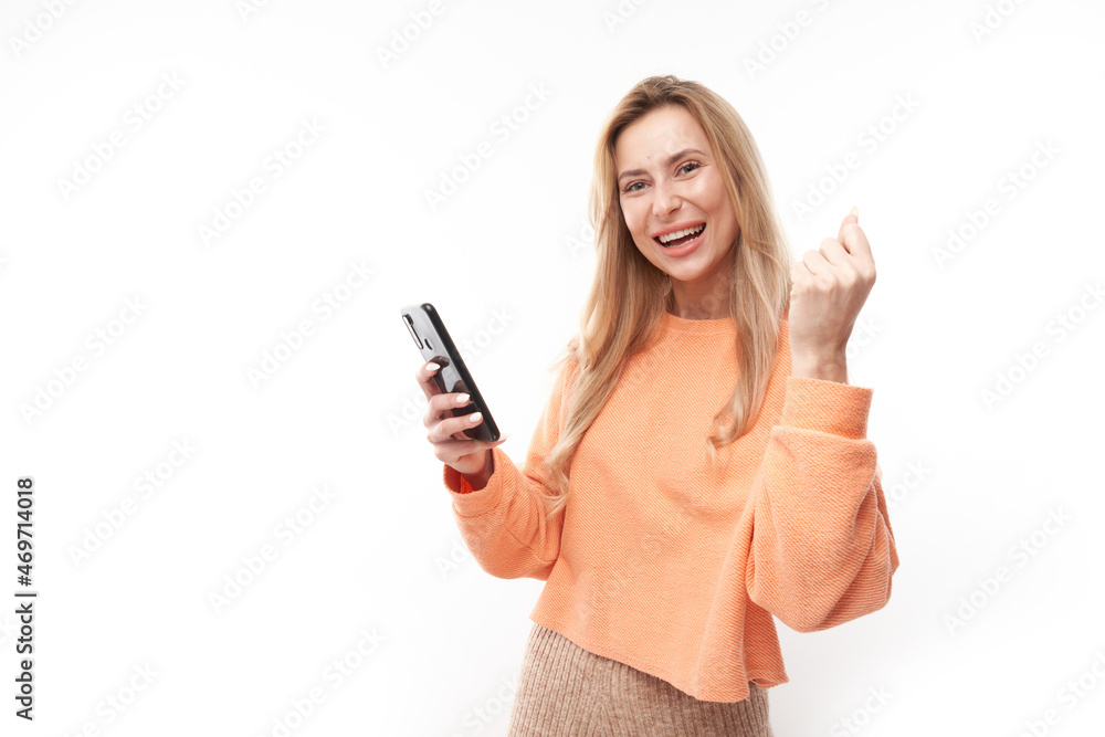 lucky smiling blond girl holding smartphone in casual isolated in white studio background received joyful message, celebrating victory lucky smiling blond girl holding smartphone in casual isolated in white studio background received joyful message, celebrating victory