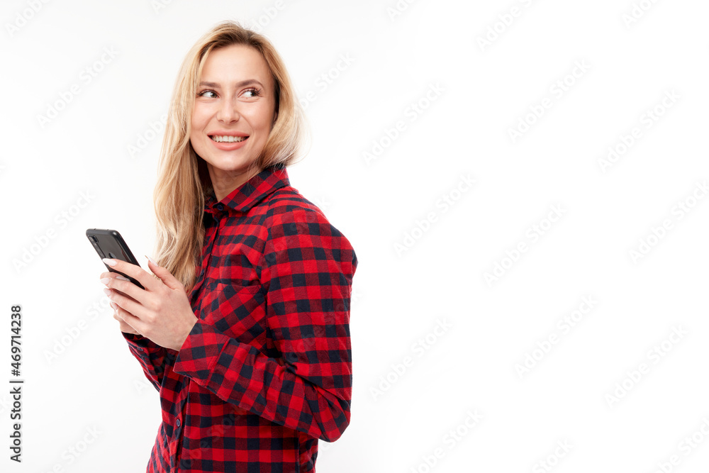 Beautiful blonde girl in casual looks at the smartphone screen and smiles isolated on white studio background Beautiful blonde girl in casual looks at the smartphone screen and smiles isolated on white studio background
