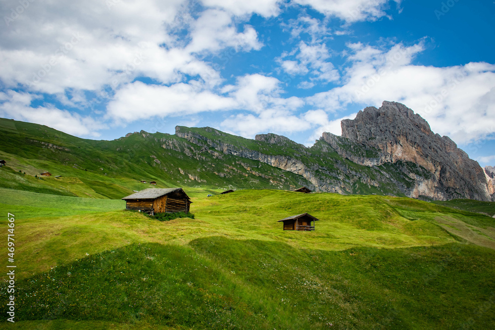 Dolomites, Italy, August 2017, in the valley against the background of mountains and blue sky on the slope of a green hill stands a wooden house