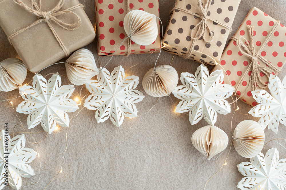 Fototapeta premium Beige paper gift boxes on a beige carpet lights Christmas garland and Christmas decorations made of paper. New Years celebration concept.