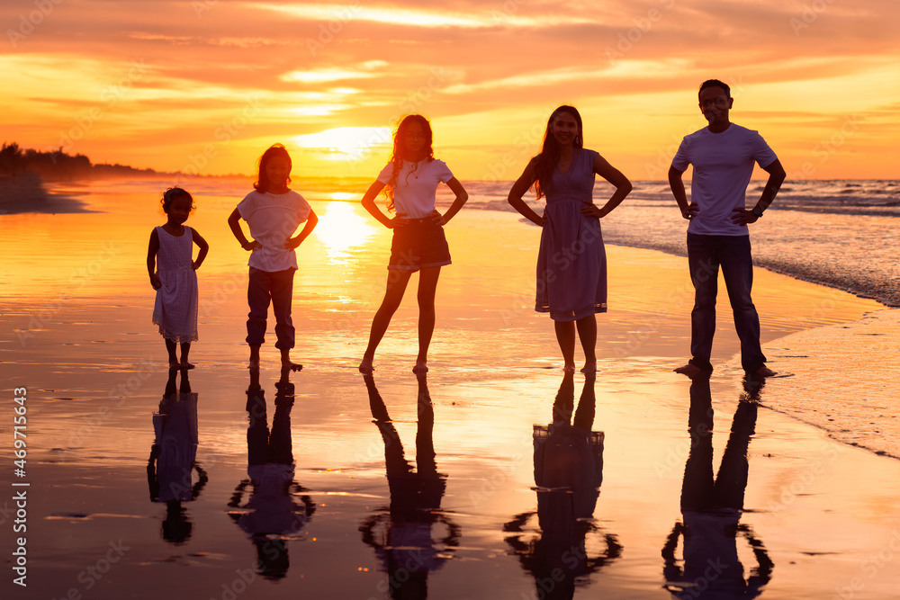 Silhouette of happy diversity generation family holding hands on hips and having fun together on tropical beach at golden sunset