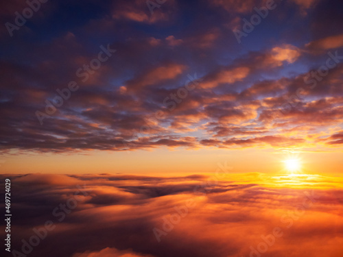 Beautiful landscape of setting sun from the sky. Dramatic sunset from the plane above bright clouds © Vitalii