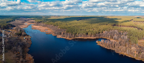 Aerial view over the lake near pine forest and small village. Autumn photo of a lake with clean water reflecting the sky